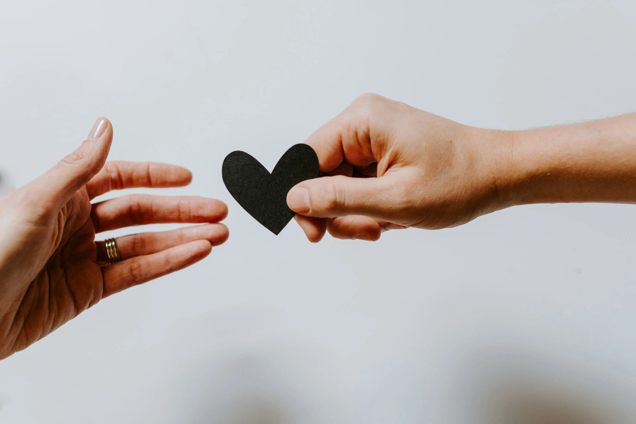 Two hands passing a black paper heart, offering support